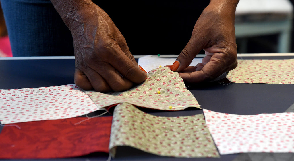 Close up of a pair of hands with red fingernail polish placing quilt squares. Image by Mark Almond.