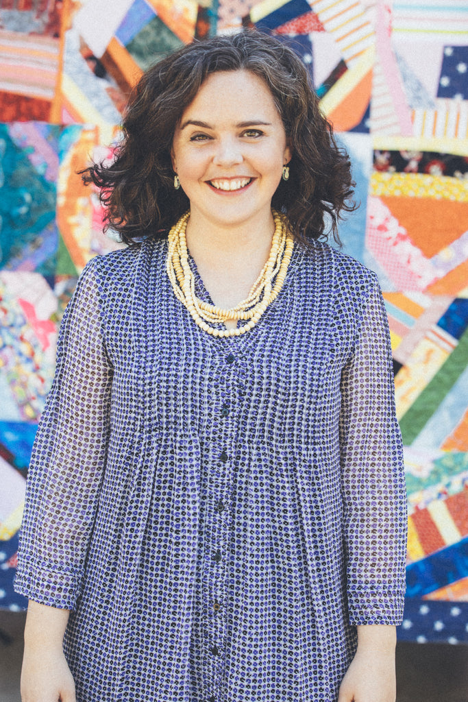 Bib & Tucker CFO + Founder Lillis Taylor stands smiling in front of a brightly colored quilt.